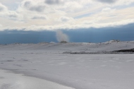 Wave-formed sand dunes line the edge of the floe; waves crashing up onto the ice floe from open water behind it.